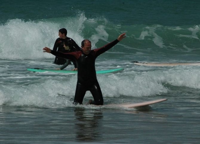 hombre de rodillas en una tabla de surf con otros chicos detras de el